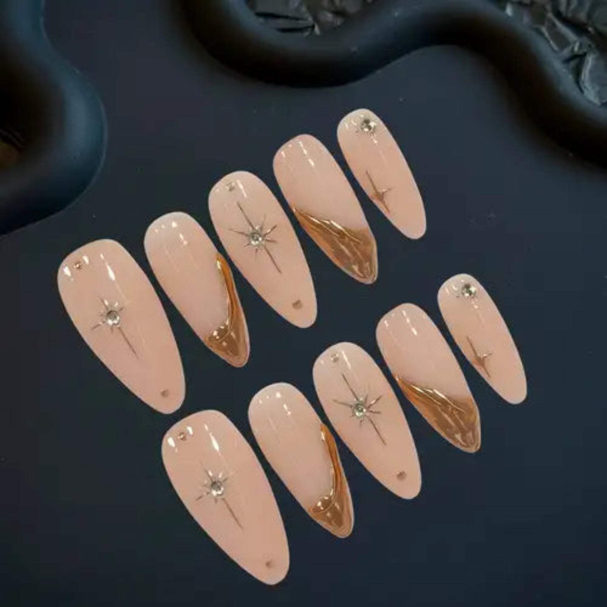 Set of beige nail extensions with gold and crystal decorations on a dark surface