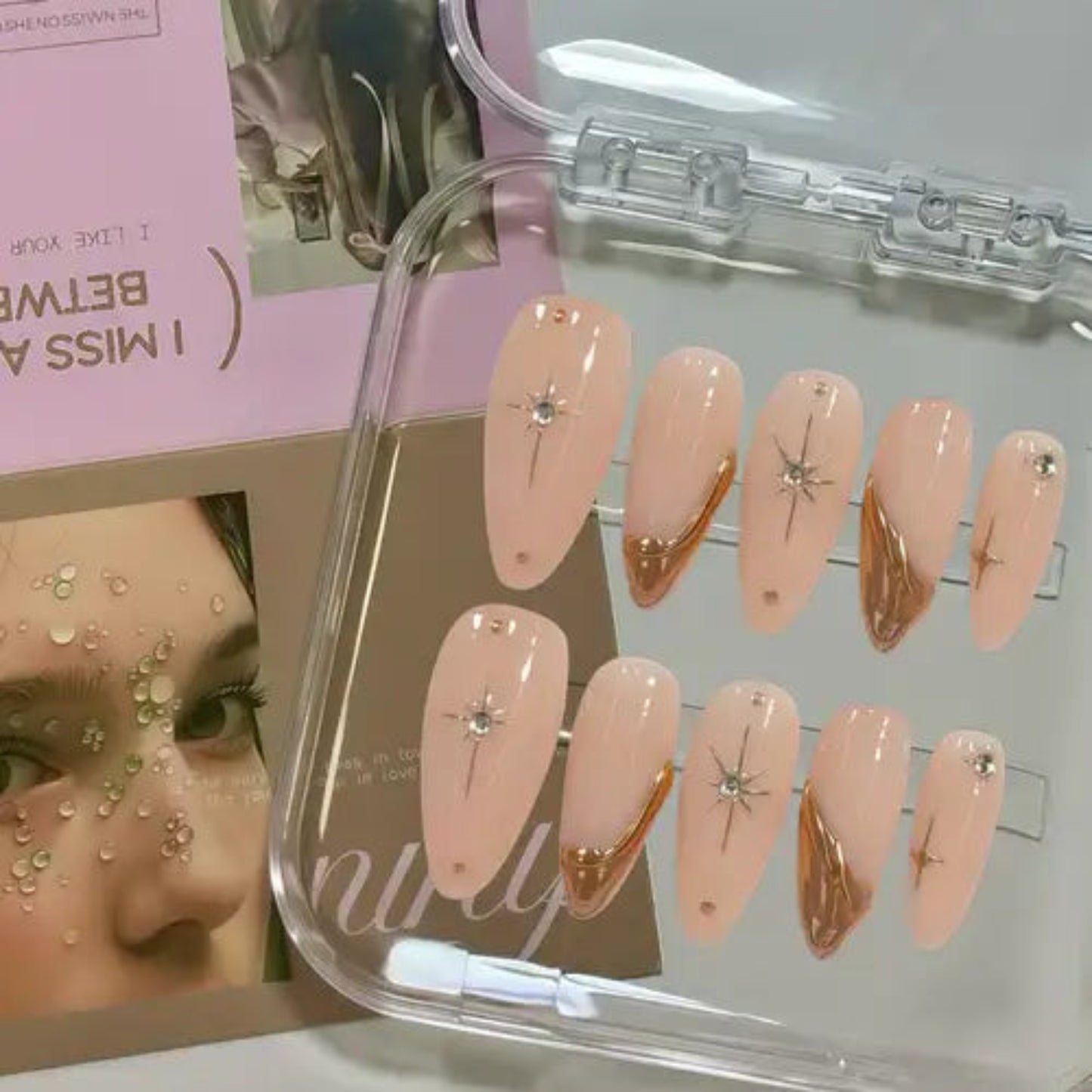 Set of pink nail extensions with gold and silver decorations in a clear case.