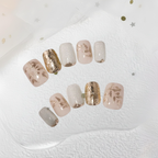 Set of decorative nails with gold and beige finishes on a textured white surface.