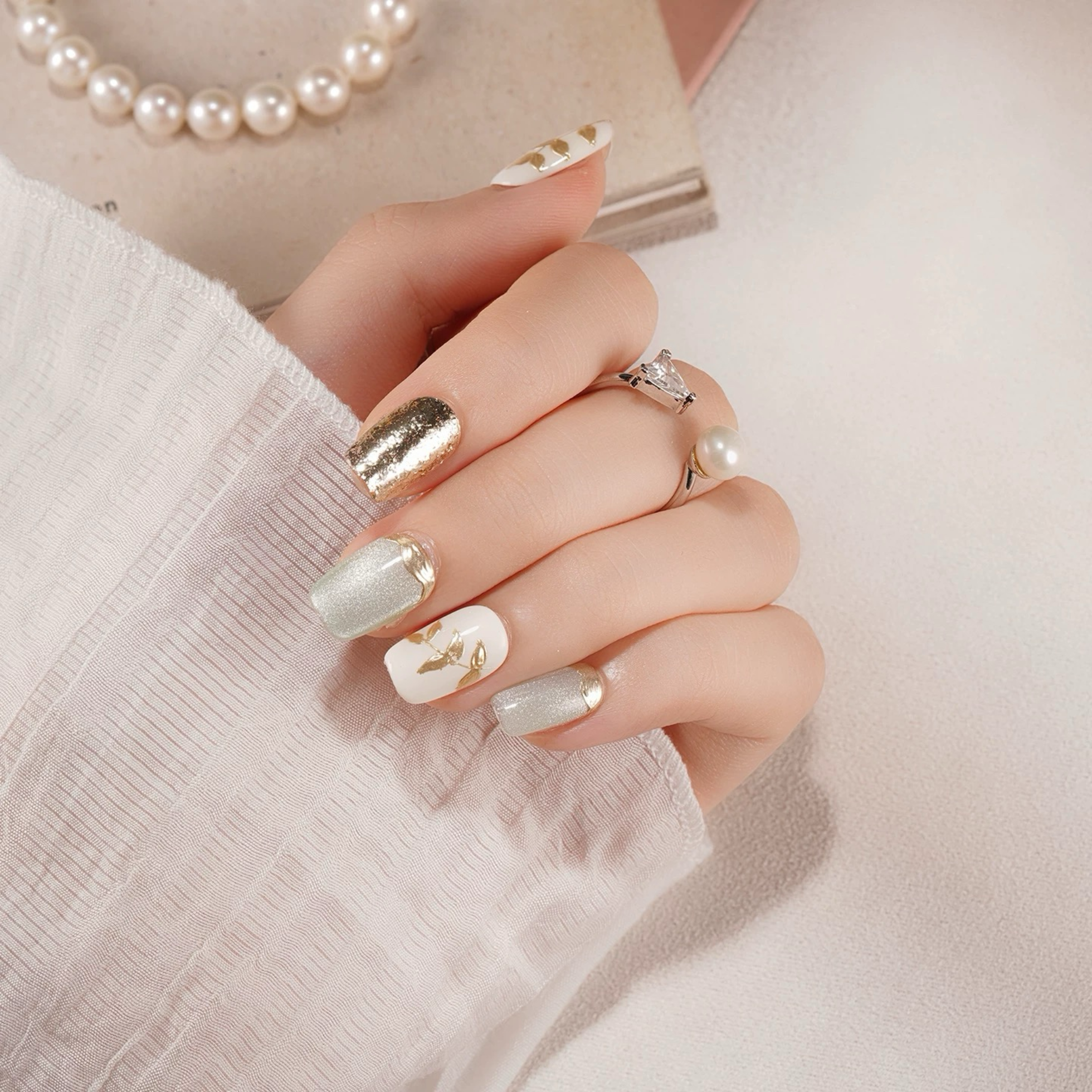 Hand with white and gold nail polish wearing a pearl necklace on a light background