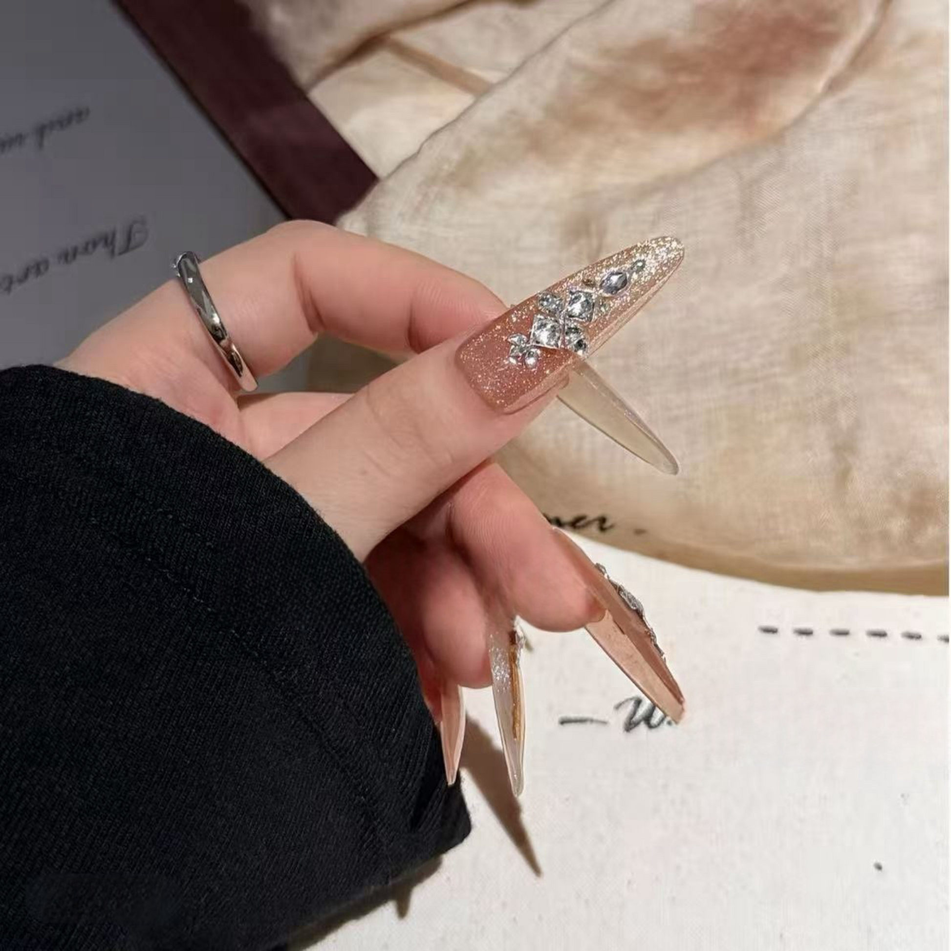 Hand holding a rose gold stiletto with rhinestone details against a blurred background