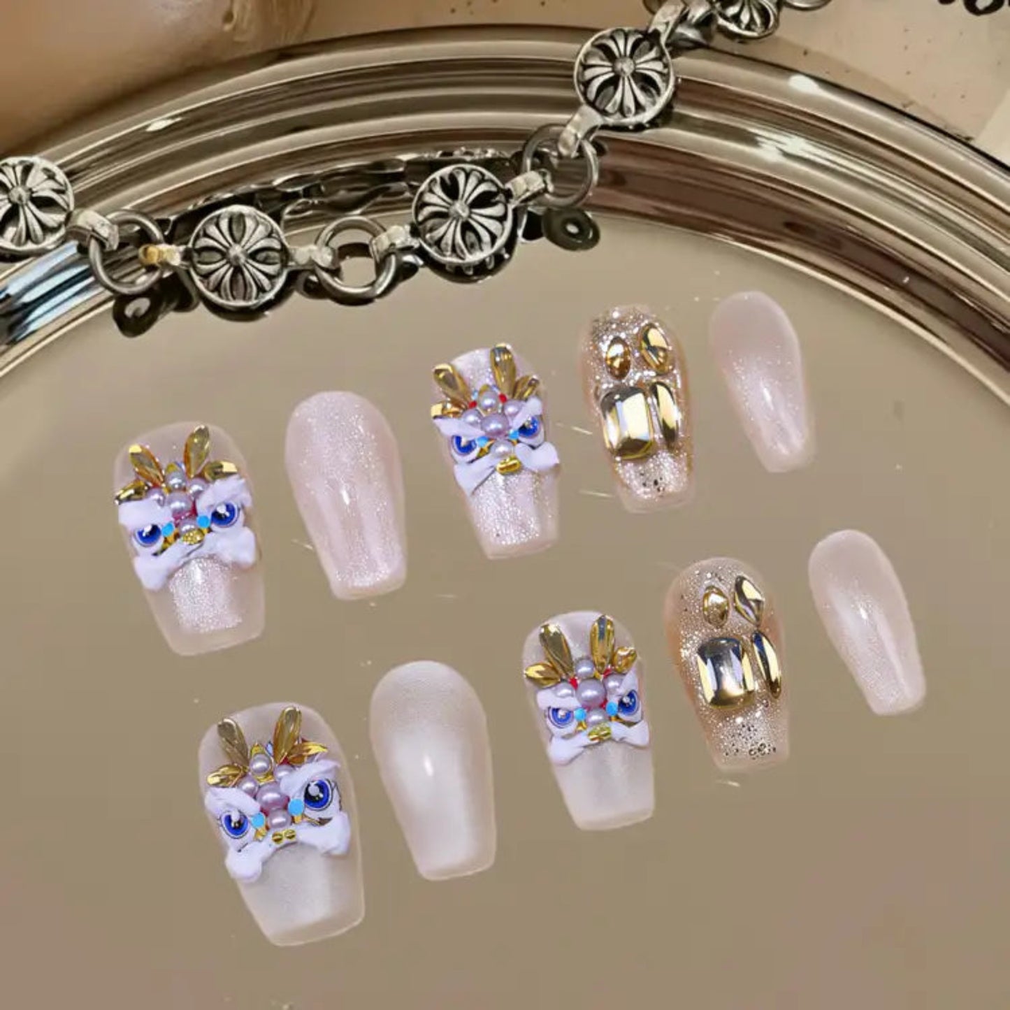 Decorative false nails with gold and white designs on a reflective surface.