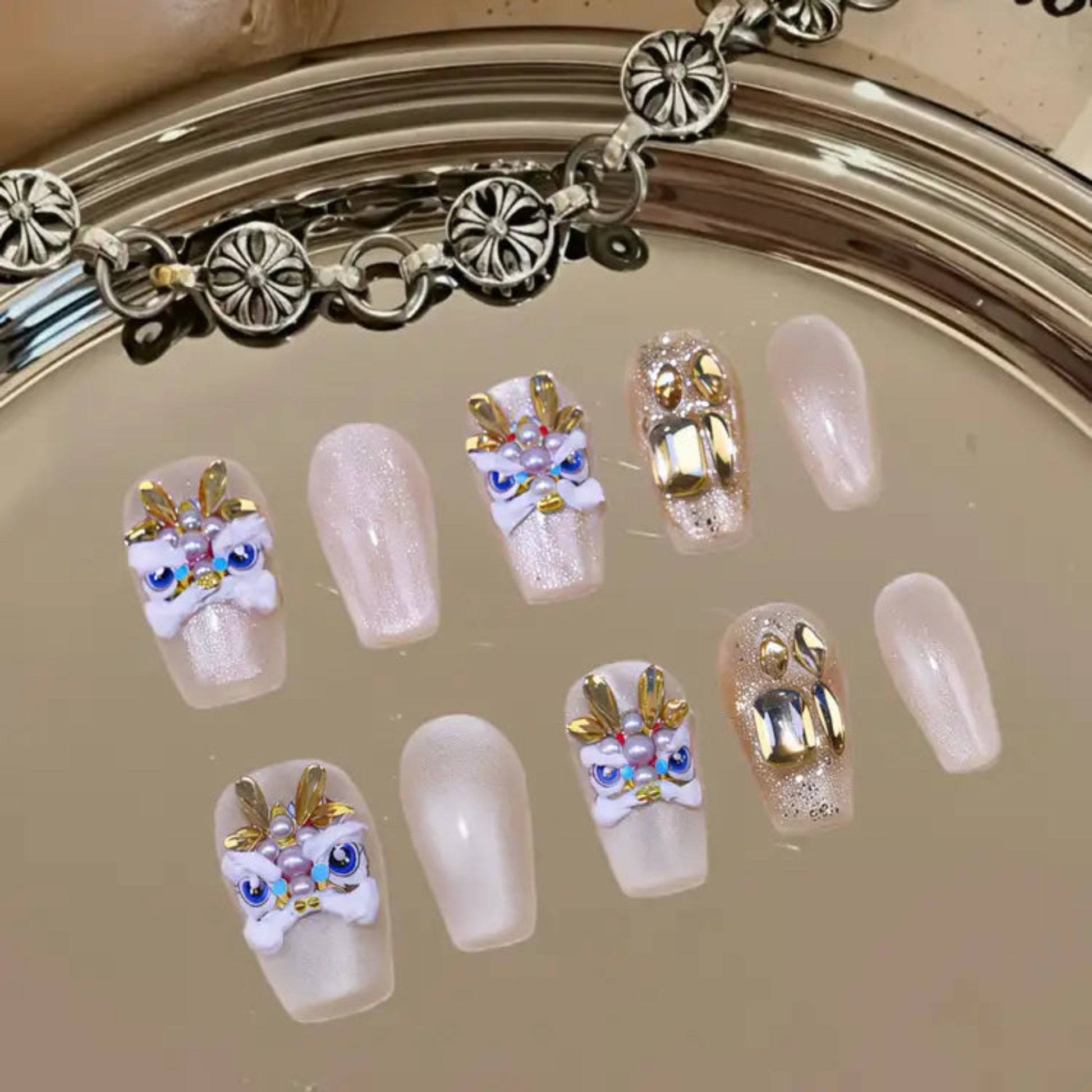 Decorative false nails with gold and white designs on a reflective surface.