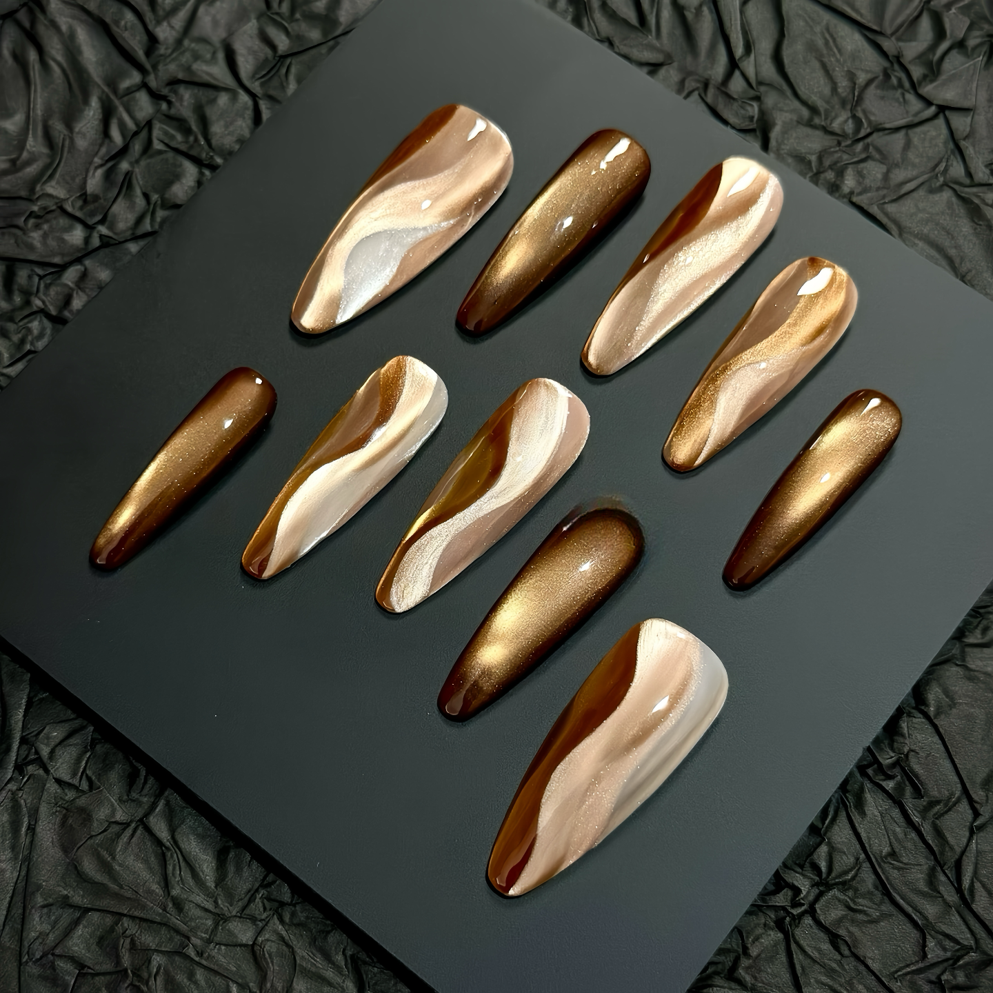 Gold and bronze nail art designs on a dark surface