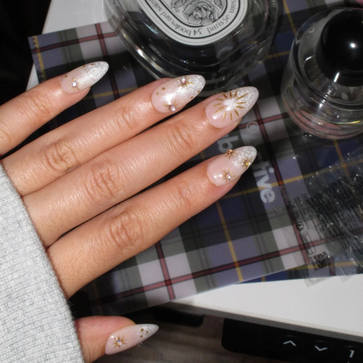 Hand with decorative nails on a checkered tablecloth with nail polish bottles.