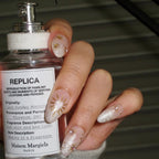 Hand holding a Maison Margiela perfume bottle with decorative nails.