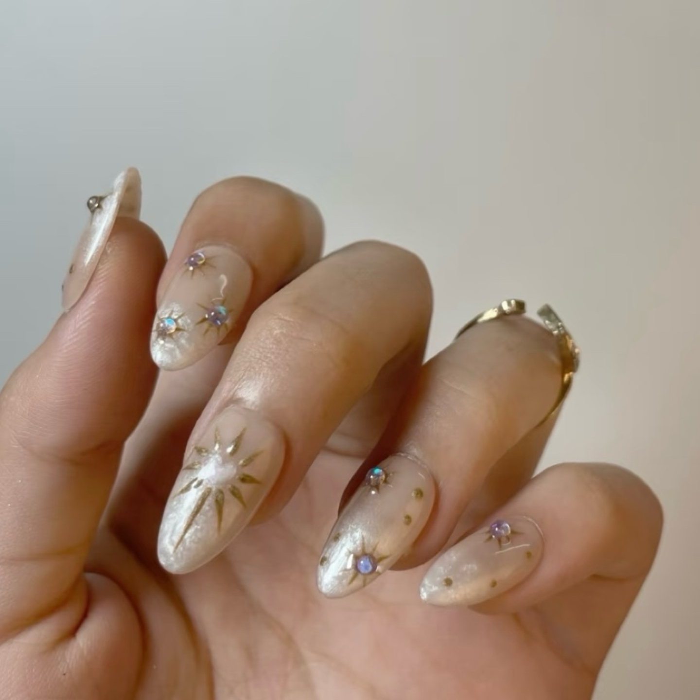 Hand with decorative nails featuring pearls and small gemstones on a neutral background