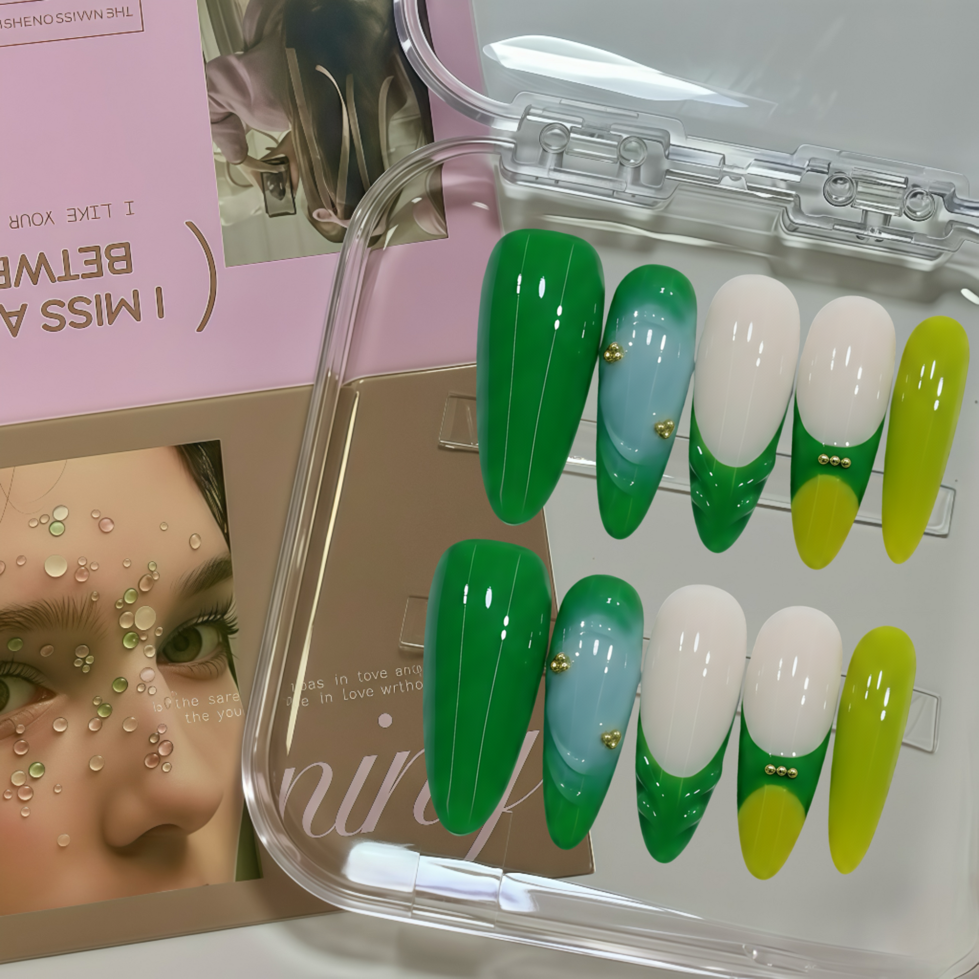 Set of green, white, and yellow false nails in a clear case with a magazine in the background.