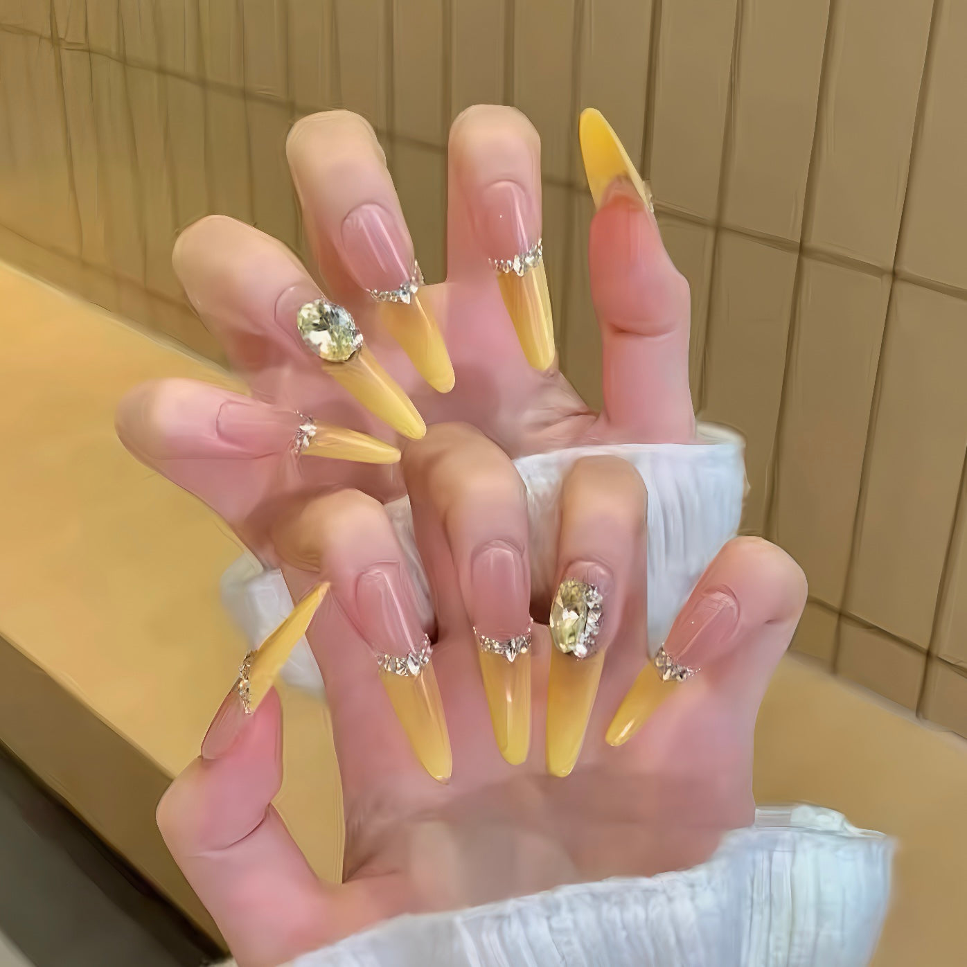 Hand with yellow acrylic nails and rhinestone decorations against a neutral background