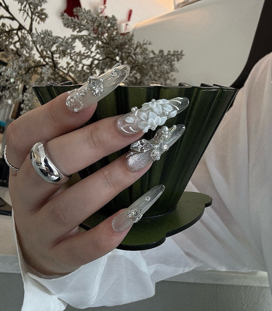 Hand holding a black stand with decorative nail art pieces against a blurred indoor background
