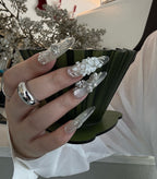 Hand holding a black stand with decorative nail art pieces against a blurred indoor background