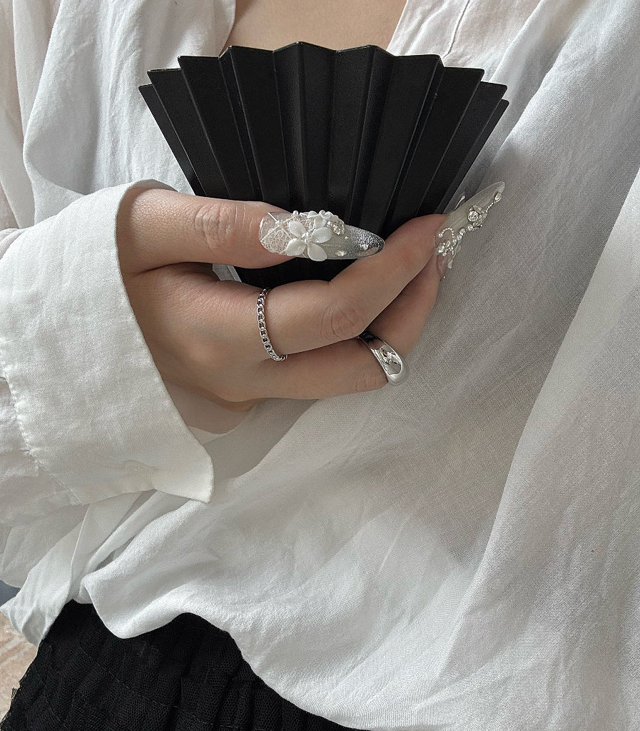 Person holding a black fan with white lace details, wearing a white shirt.