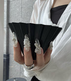 Person holding a black fan with decorative rings on fingers against a neutral background