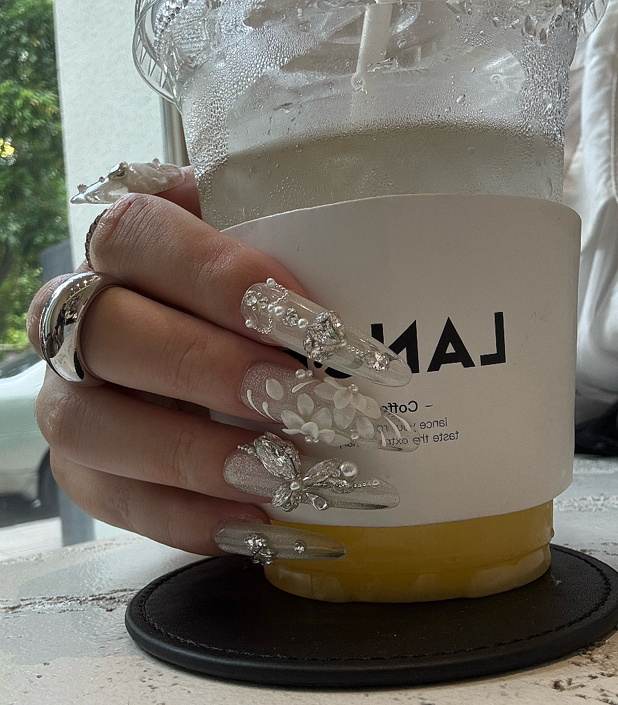 Hand holding a coffee cup with decorative nails and a ring.