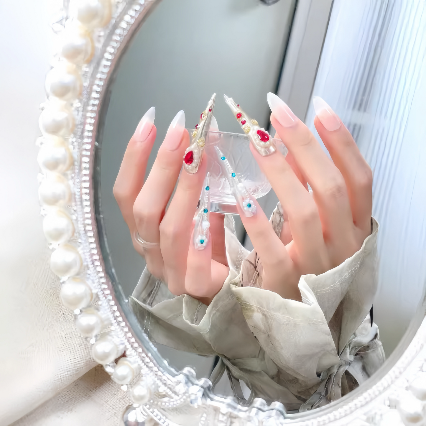 Close-up of hands with decorative nails in front of a round mirror with a pearl frame.