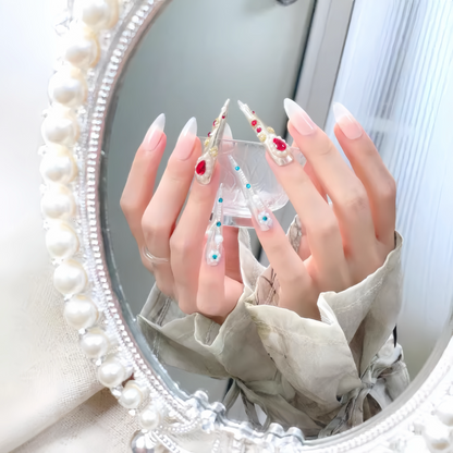 Close-up of hands with decorative nails in front of a round mirror with a pearl frame.