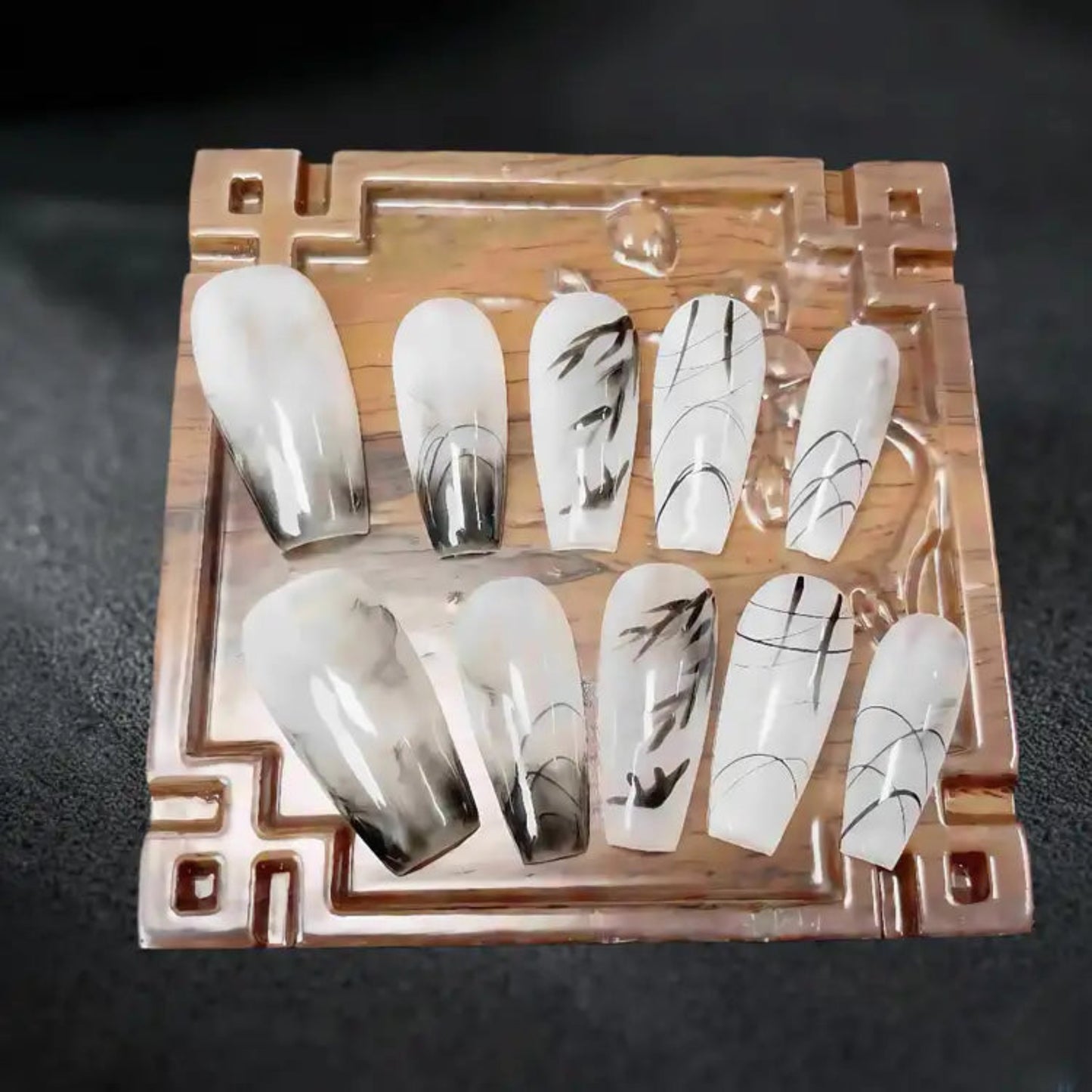 Set of white and black nail art designs on a wooden display stand.