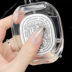 Clear perfume bottle with decorative label held by a hand against a dark background