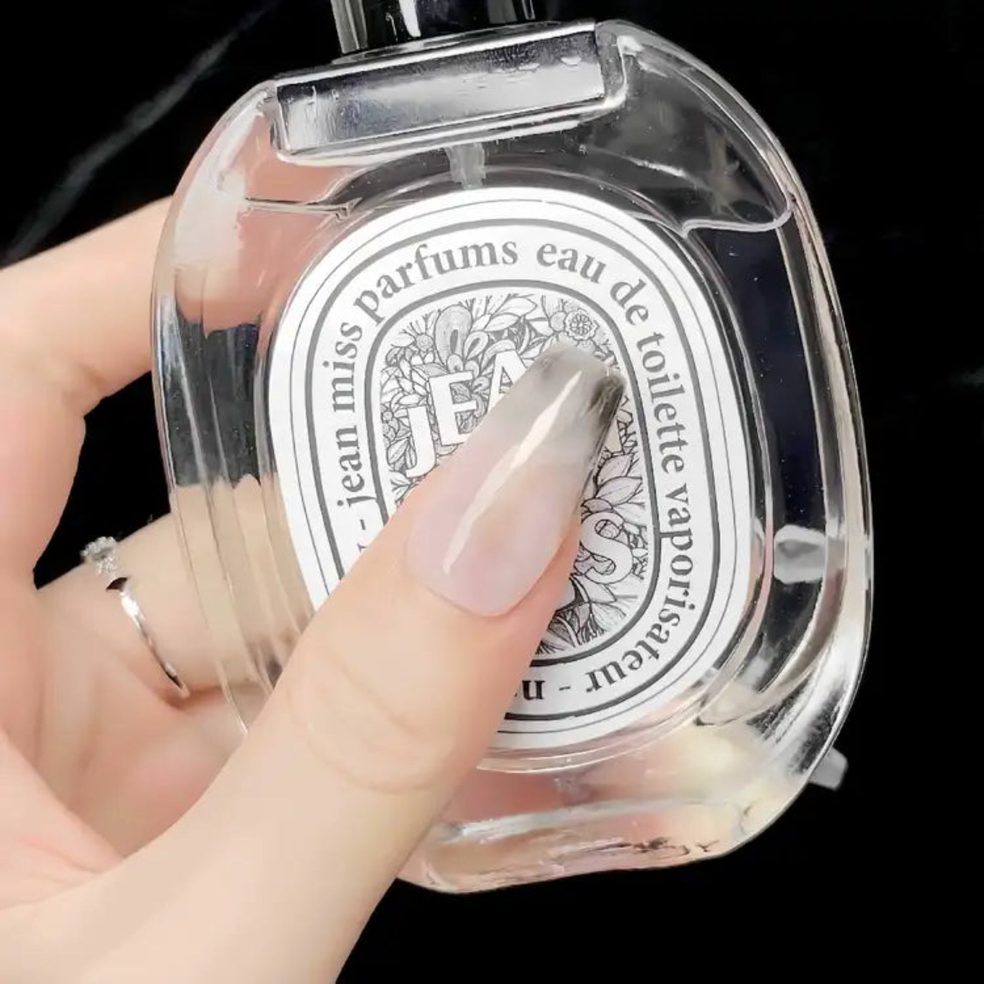 Clear perfume bottle with decorative label held by a hand against a dark background