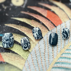 Black and white patterned earrings on a colorful leaf-like background