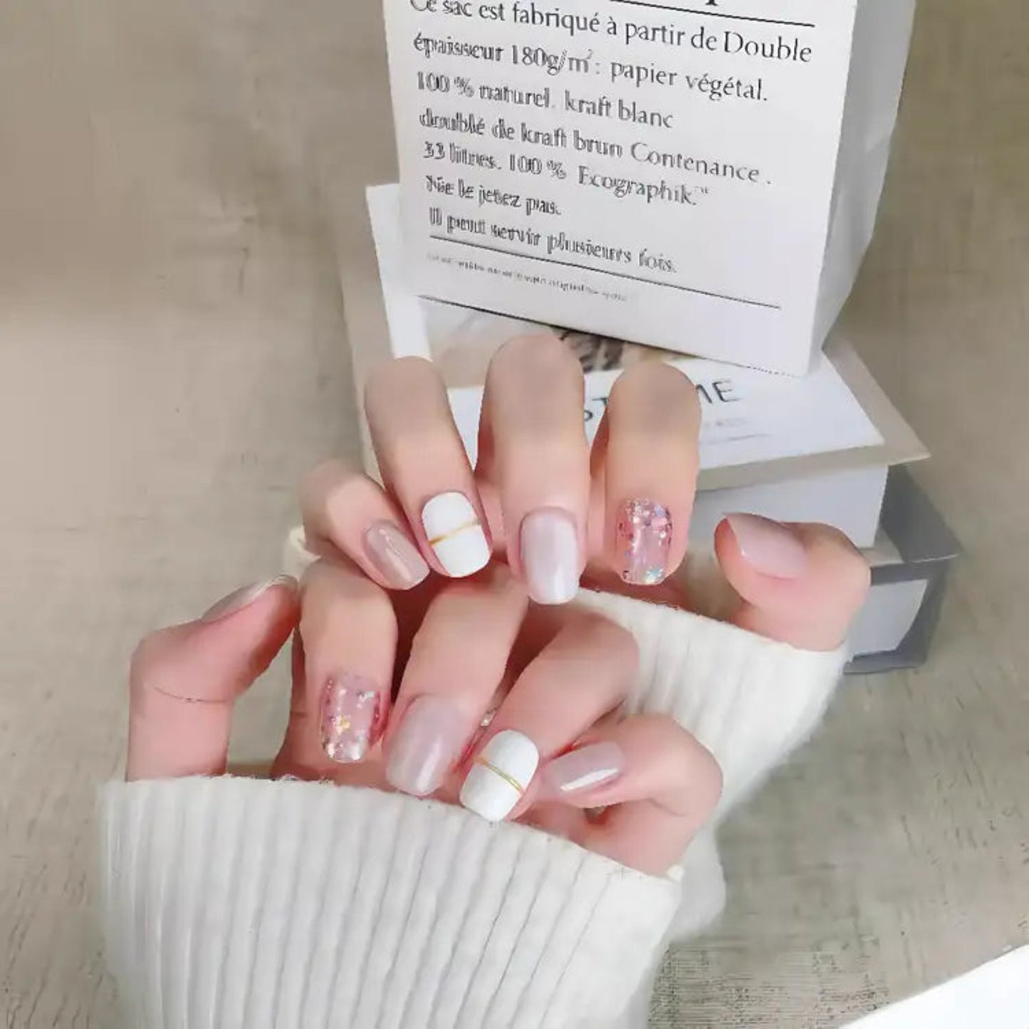 Hand with stylish nail design holding a box on a light wooden surface