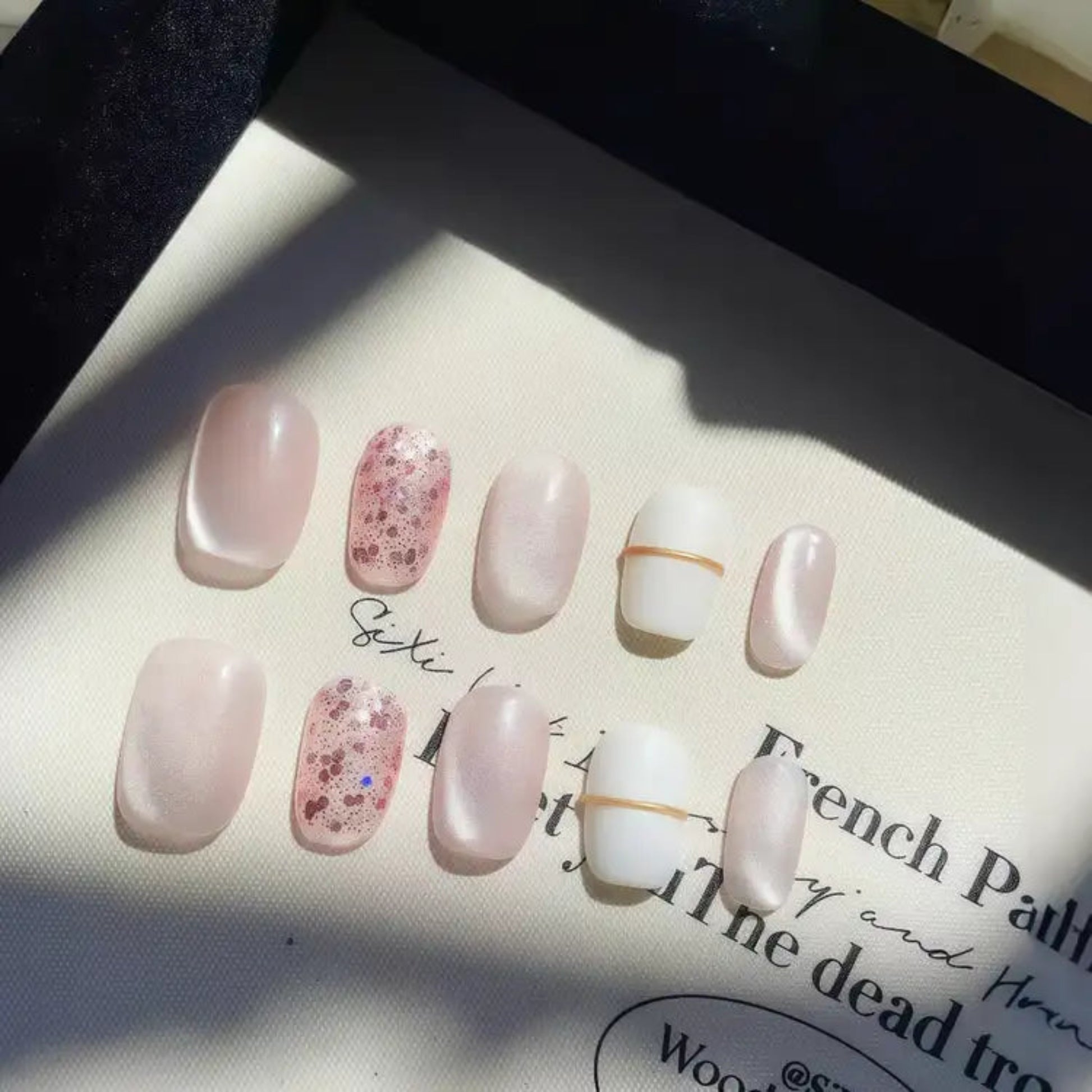 Set of pink and white nail samples on a textured surface with text.