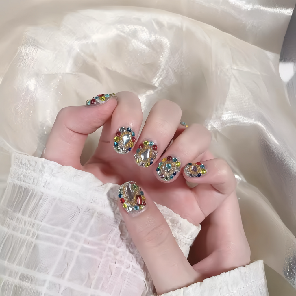 Hand with colorful rhinestone nail design against a soft white background