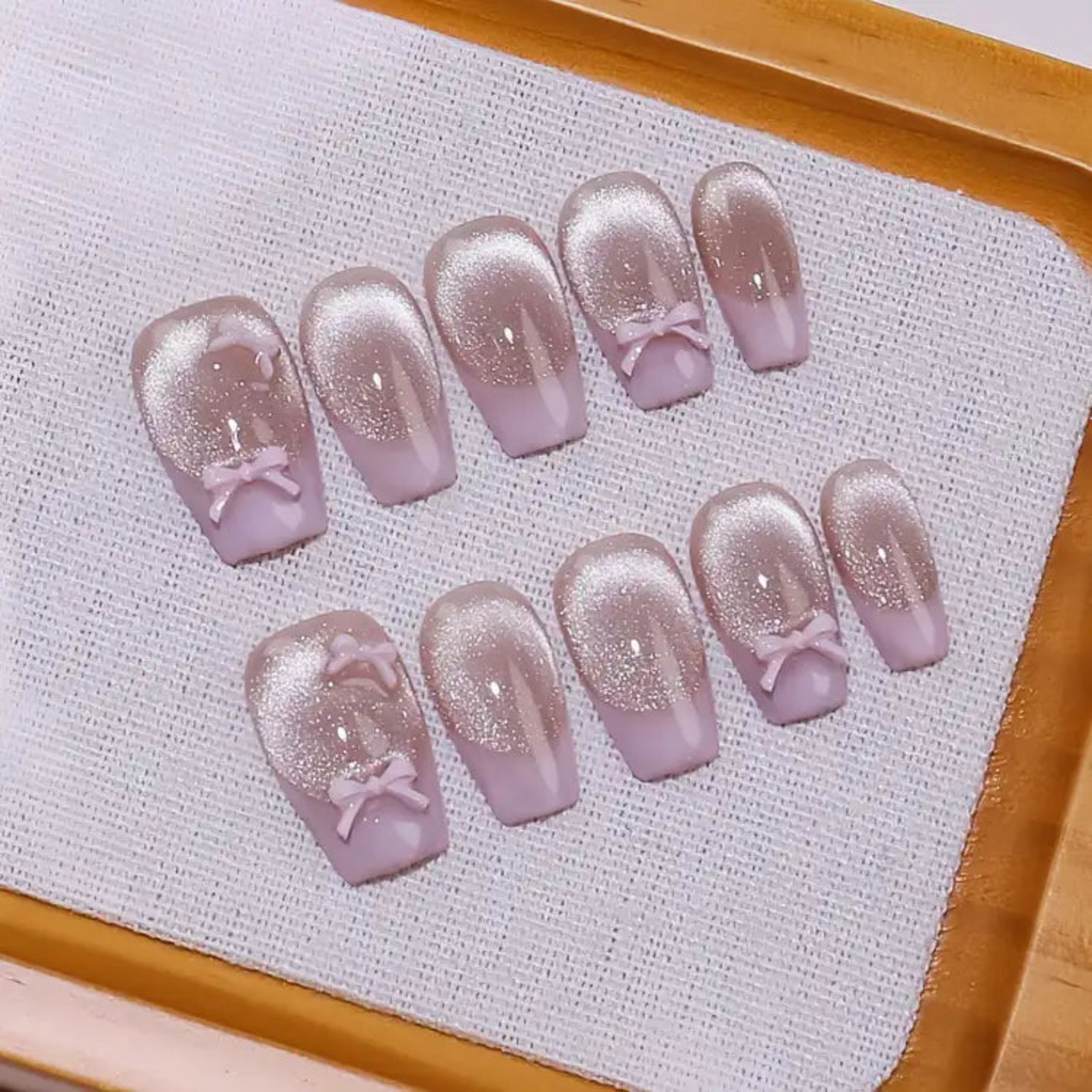 Set of purple nail art designs with bows on a textured white surface.