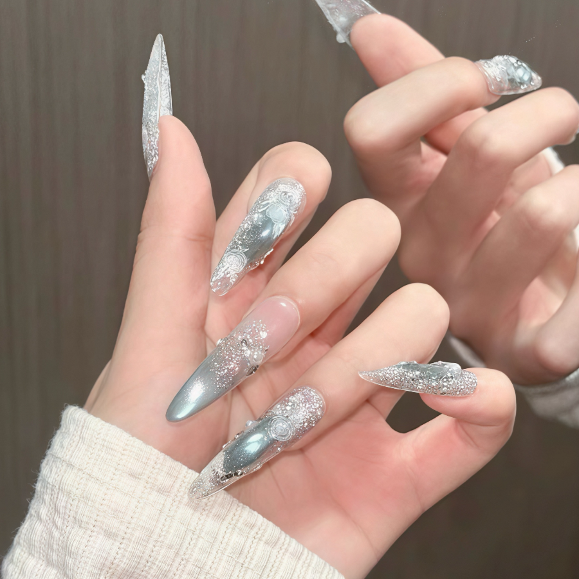 Close-up of hands with silver glittery nail designs against a neutral background
