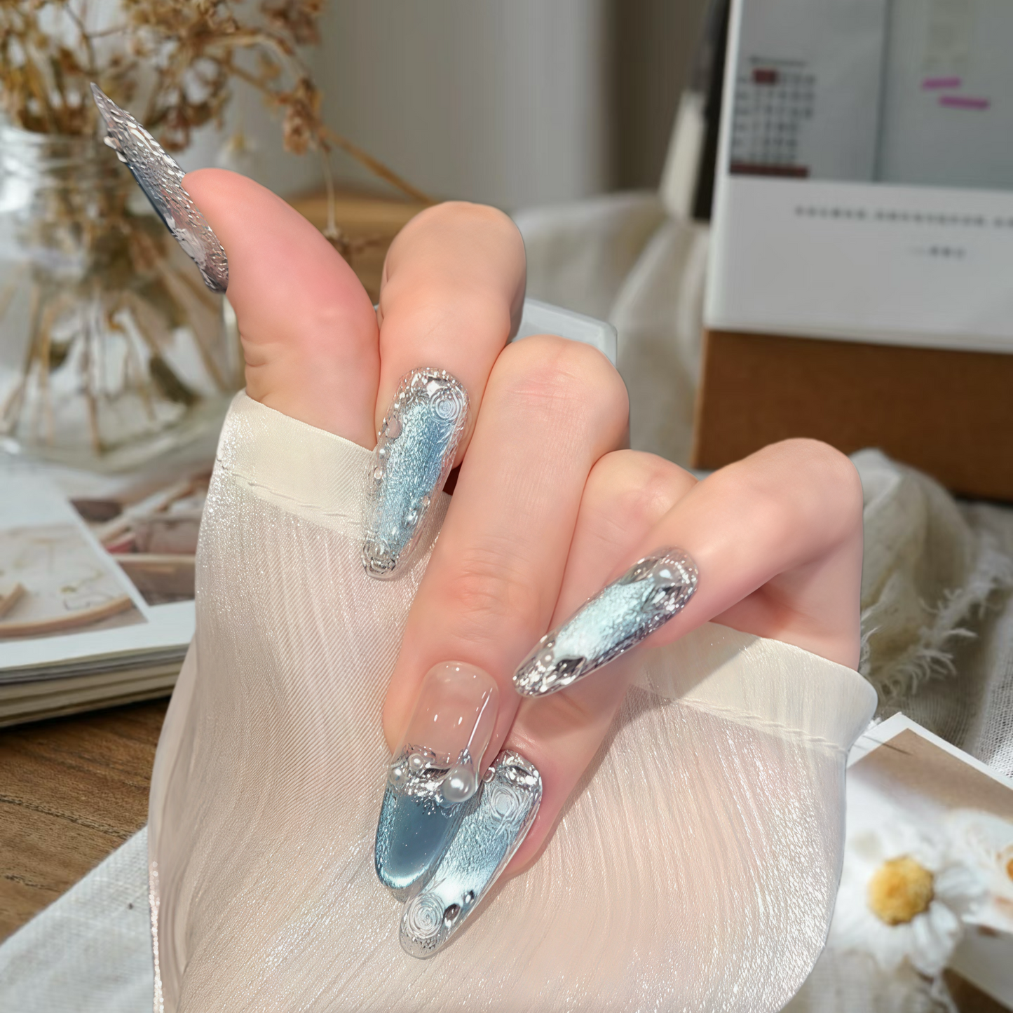 Hand with decorative nails holding a small object, blurred indoor background