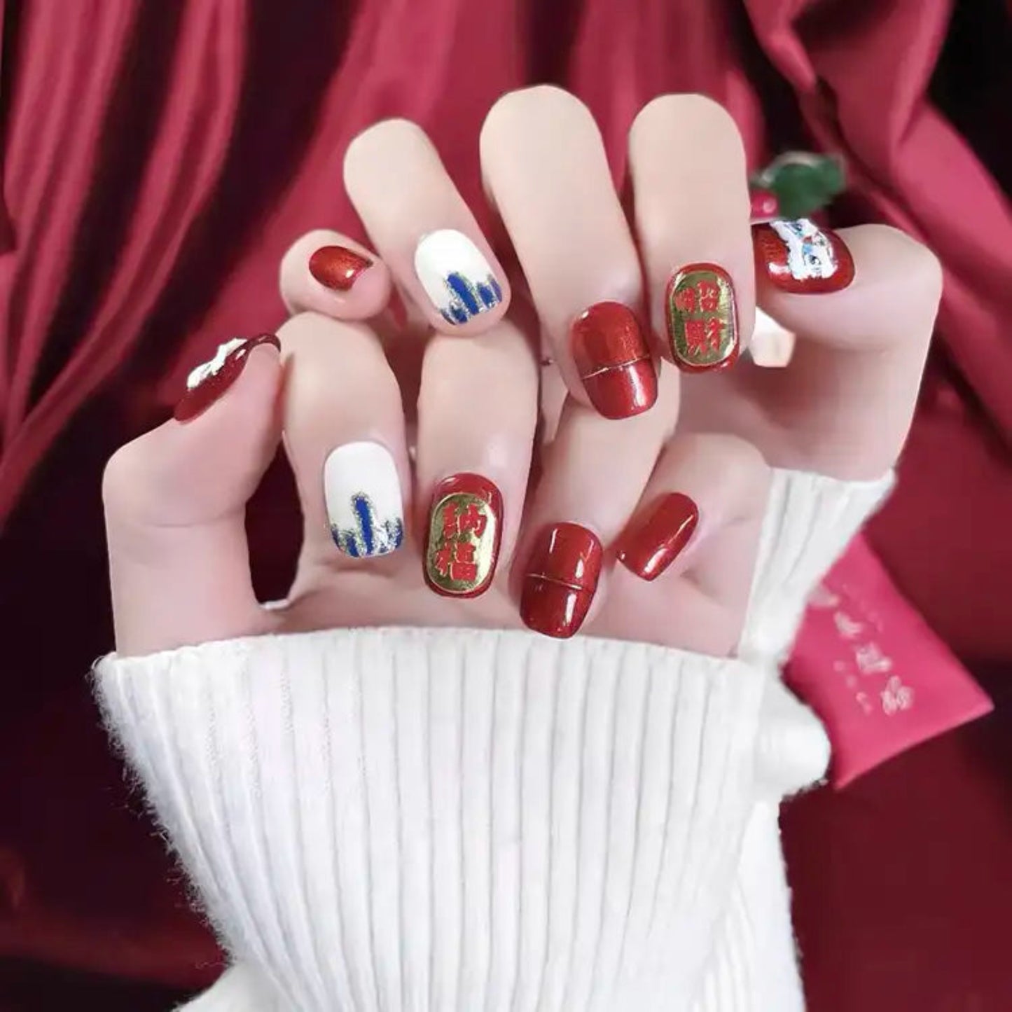 Close-up of a hand with intricately designed nails against a red background
