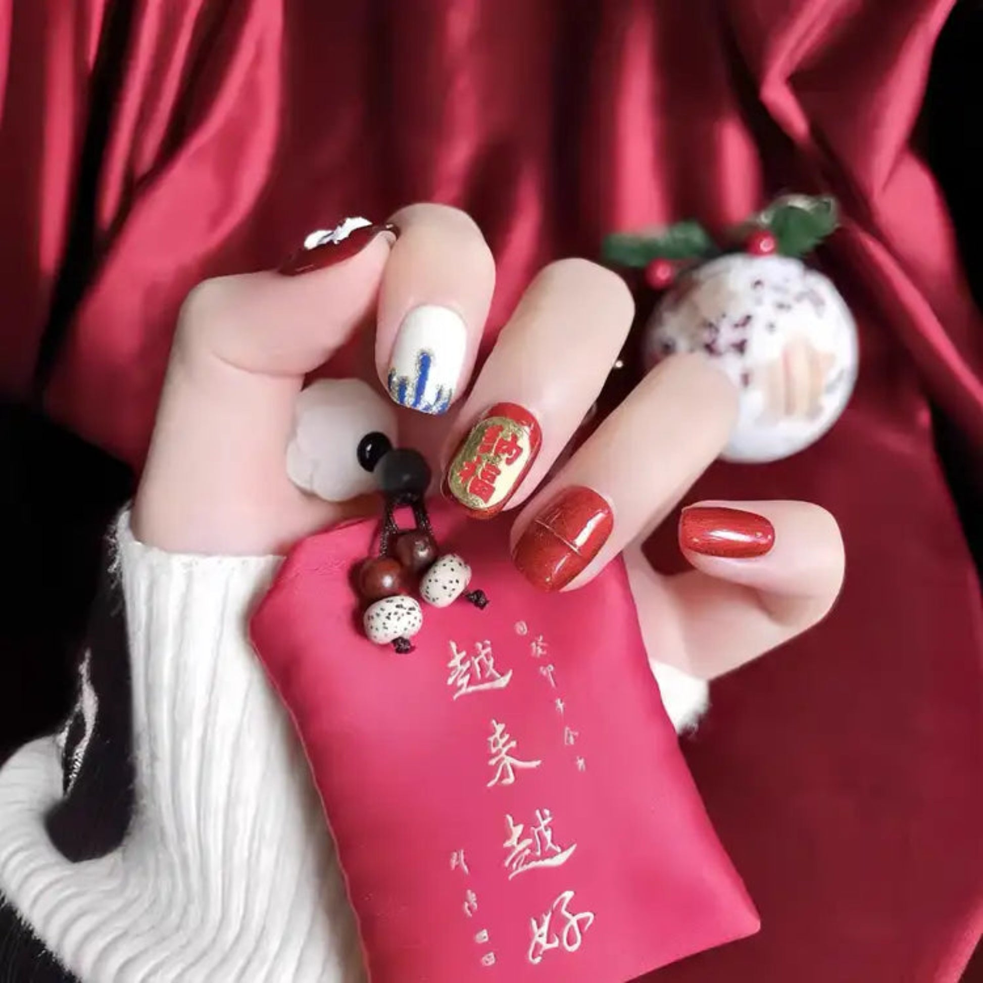 Hand with decorated nails holding a red pouch against a red fabric background