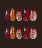 Set of red and gold nail designs with floral embellishments on a dark background