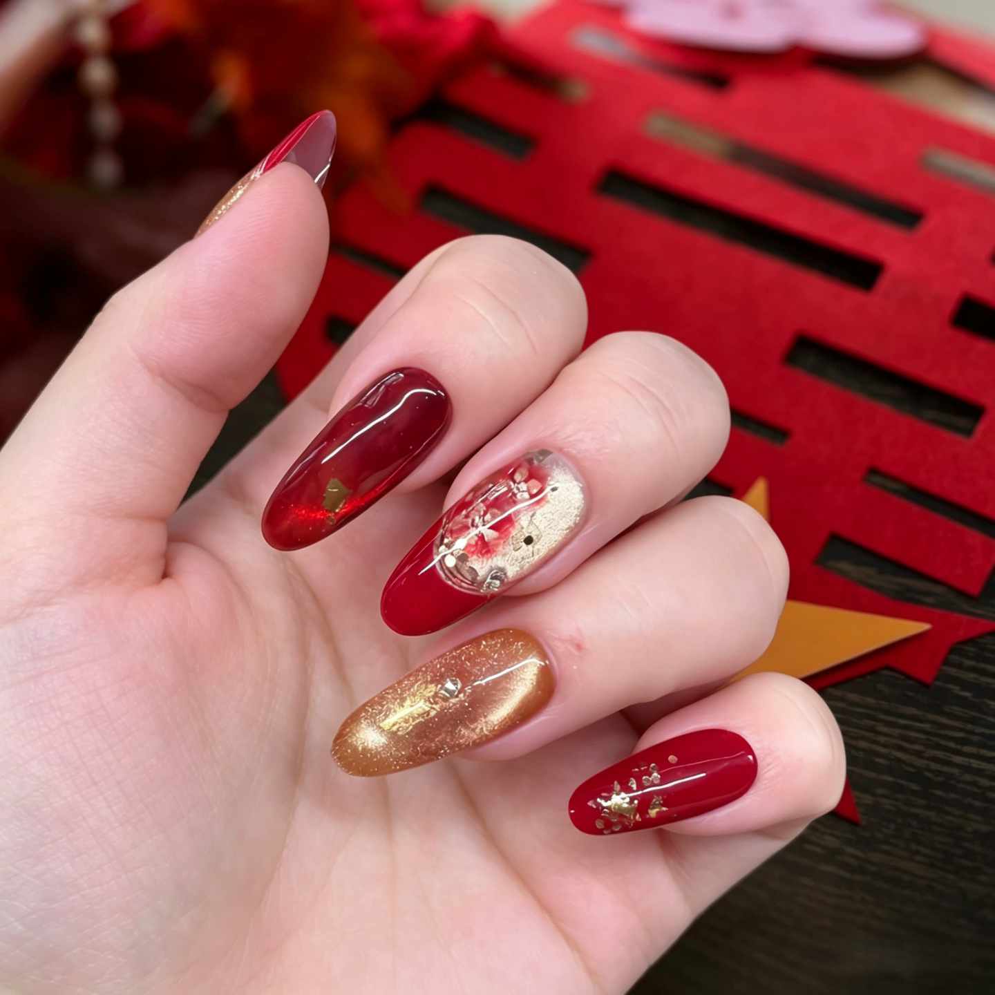 Hand with red and gold nail polish against a red decorative background