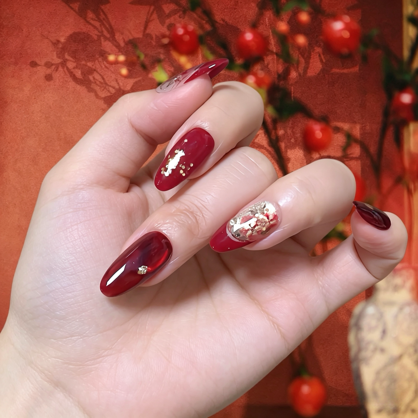 Hand with red nail polish and gold glitter on a decorative background
