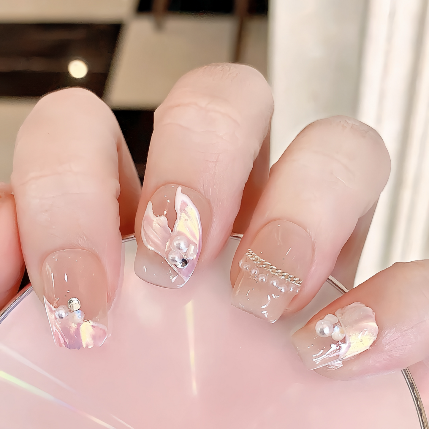 Close-up of a hand with clear nail polish and decorative elements.
