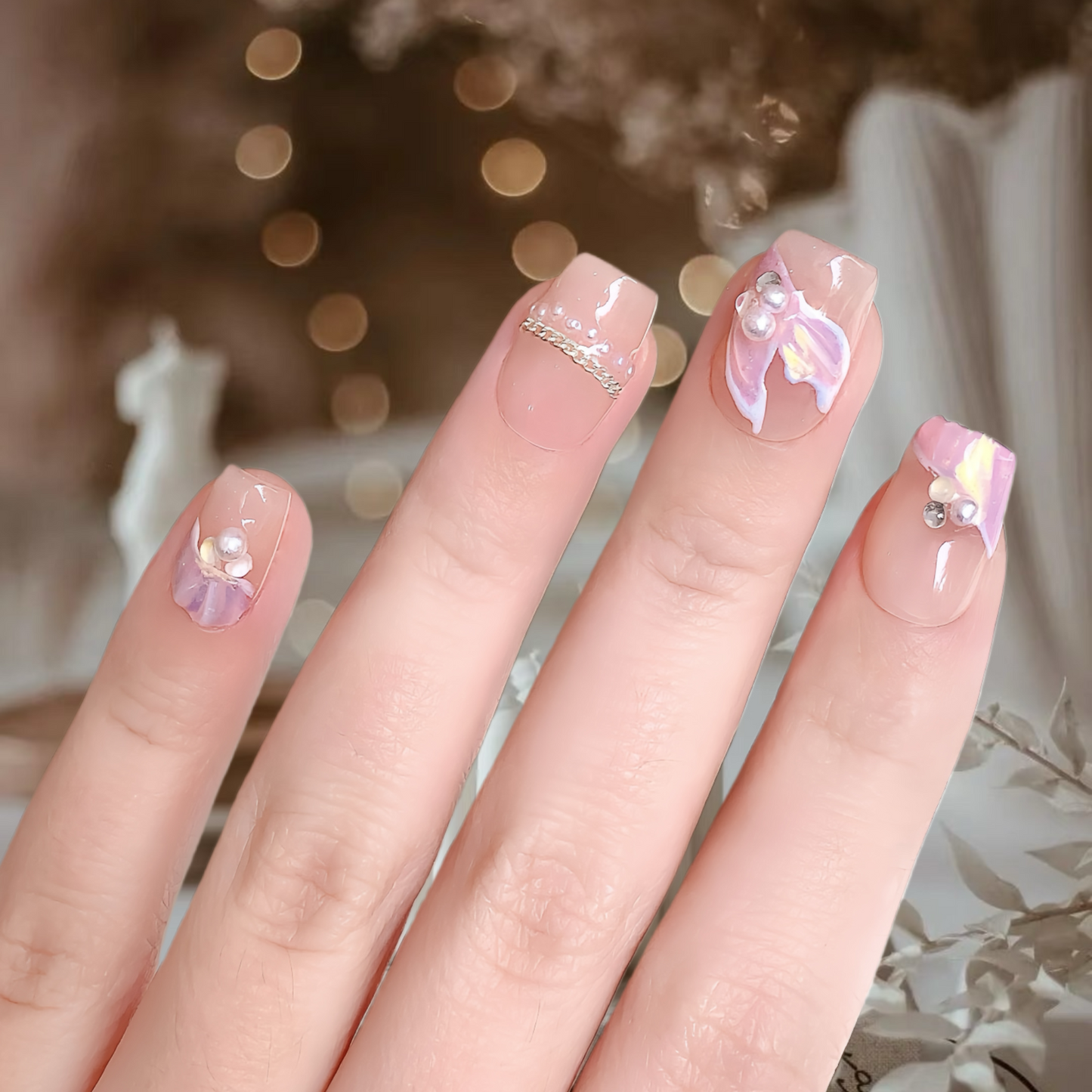 Close-up of a hand with decorative nails featuring flowers and rhinestones against a blurred background.