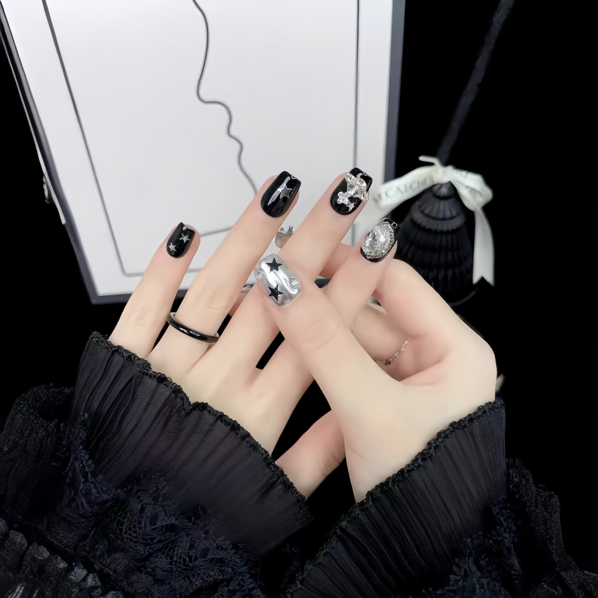 Close-up of hands with black nail polish and silver rings against a blurred background