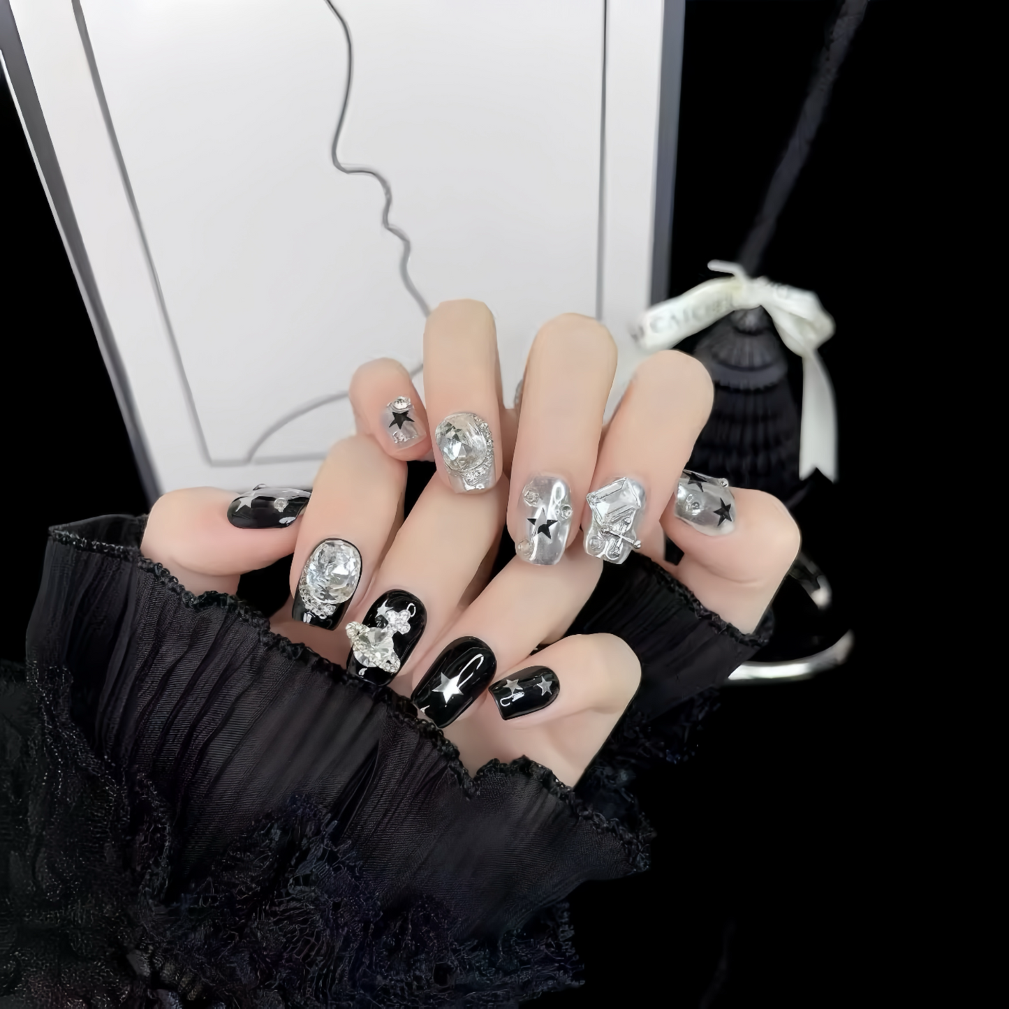 Nails with decorative designs and gemstones held by a person wearing a black sleeve.