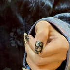 Hand with black nail art holding a metallic object against a dark background