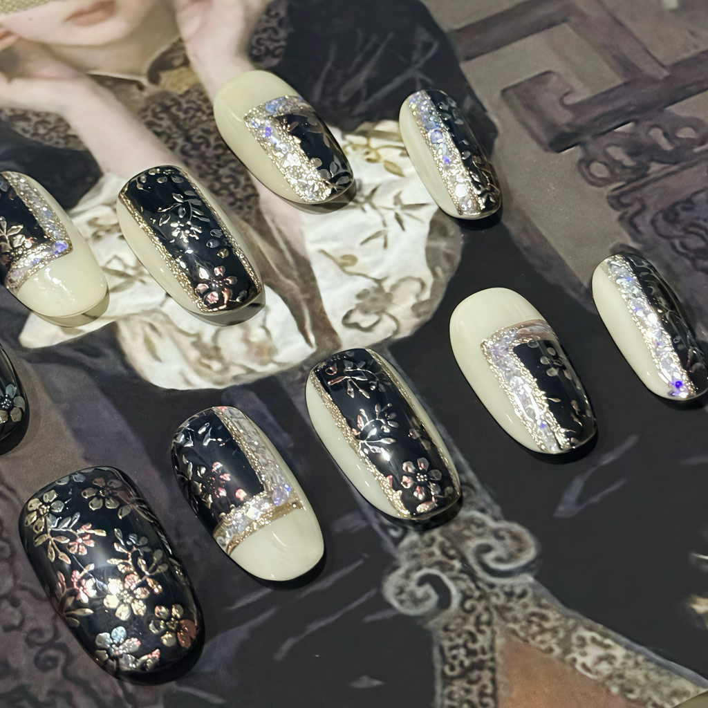 Decorative nail art with black, gold, and white designs on a patterned surface.