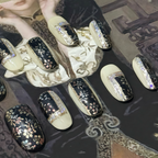 Decorative nail art with black, gold, and white designs on a patterned surface.