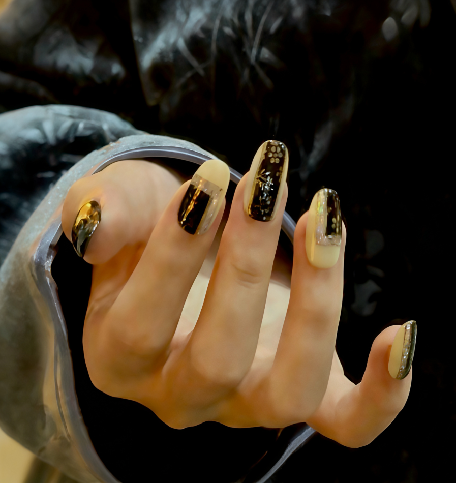 Hand with black and gold nail design holding a clear container.