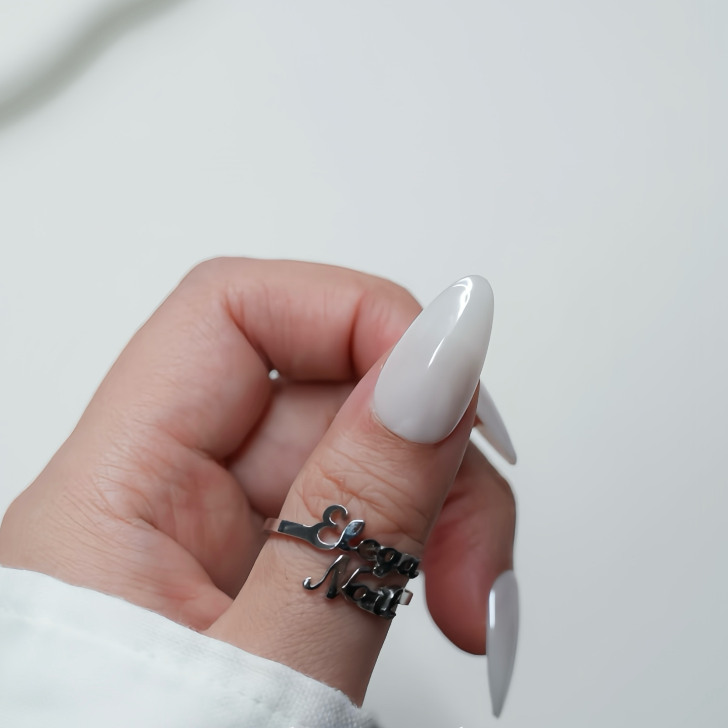 Hand with long white nails wearing multiple rings on a light background