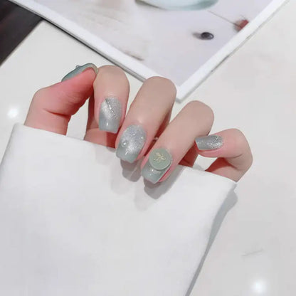 Hand with light gray nail polish and glittery accents on a white background