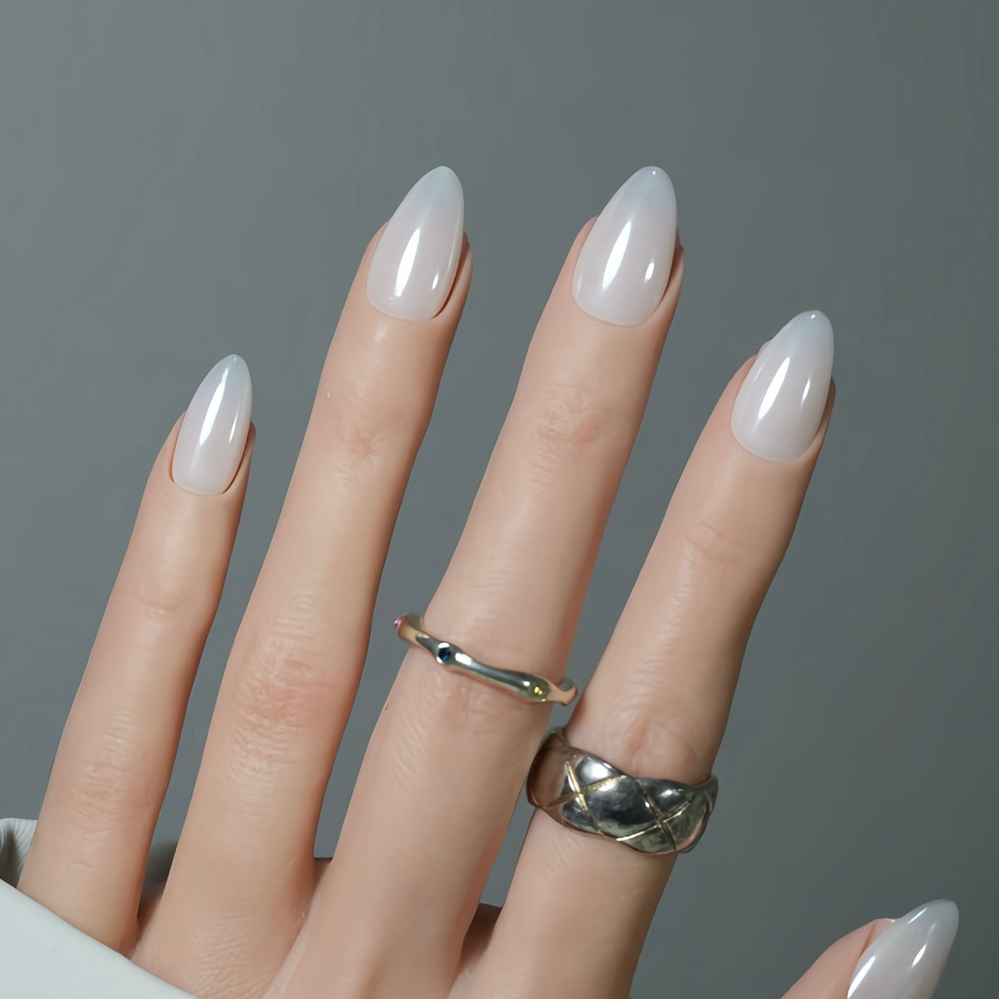 Hand with beige nail polish and silver rings on a gray background