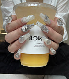 Person holding a cup with decorative nails and jewelry, wearing a white shirt.