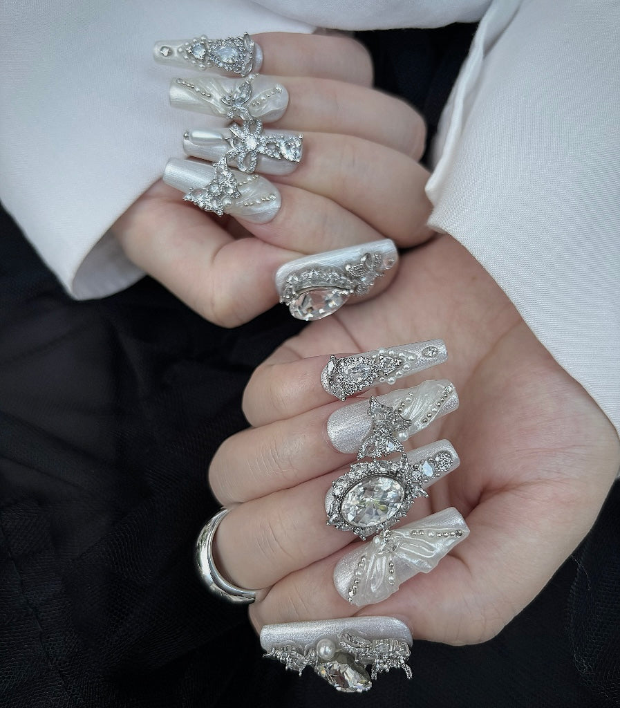 Close-up of hands with ornate nail art and jewelry against a neutral background