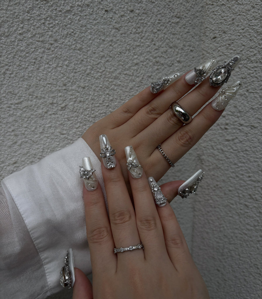 Hand with ornate nail art and jewelry against a neutral background