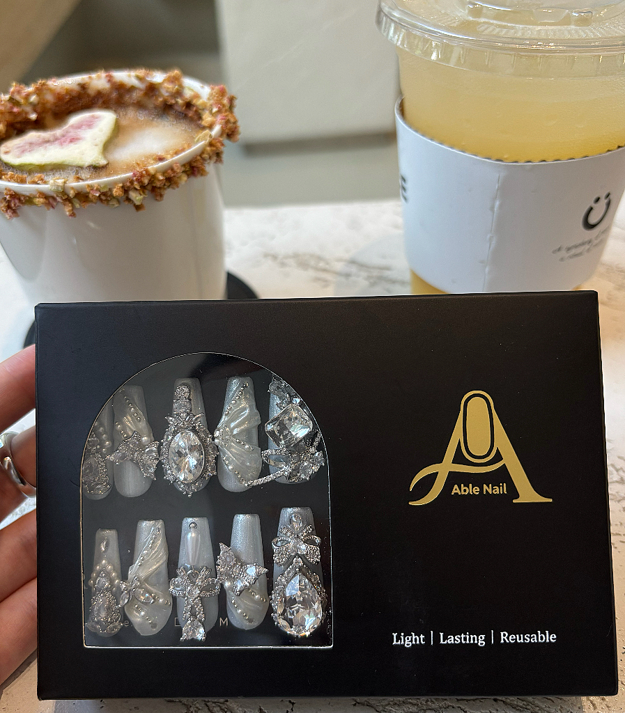 Box of decorative nails with Able Nail logo, next to a drink and dessert on a table.